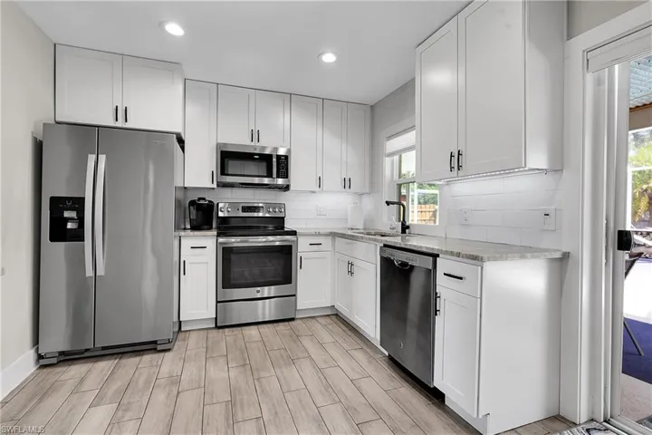 Kitchen featuring stainless steel appliances, white cabinets, wood finish floors, recessed lighting, and light stone counters