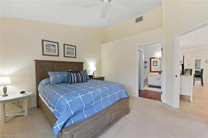 Bedroom featuring ensuite bath, ceiling fan, light colored carpet, and lofted ceiling