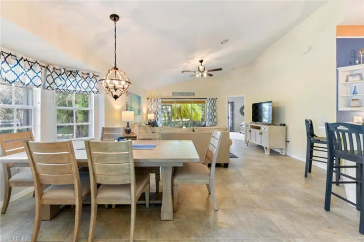 Tiled dining room with lofted ceiling and ceiling fan with notable chandelier