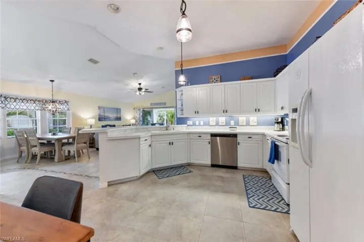 Kitchen with decorative light fixtures, a wealth of natural light, white appliances, and kitchen peninsula