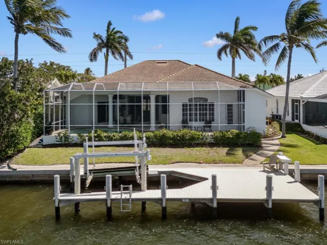Back of property with stucco siding, glass enclosure, a water view, boat lift, and a tile roof