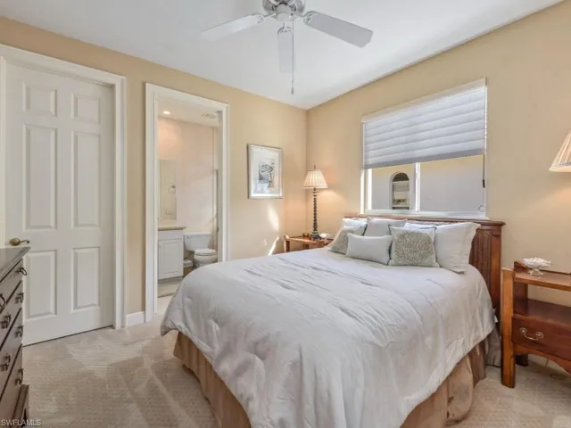 Bedroom featuring a ceiling fan, light colored carpet, baseboards, and ensuite bathroom