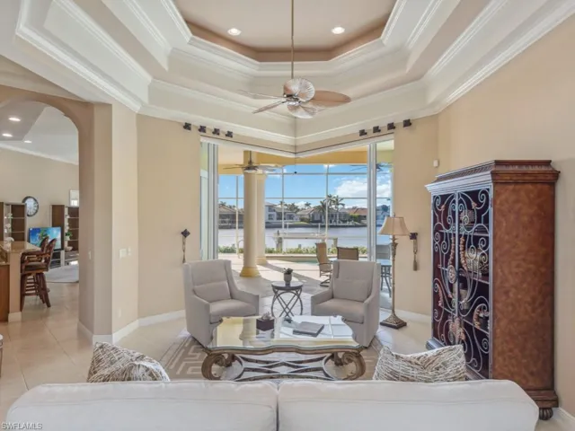 Living room featuring arched walkways, a water view, ceiling fan, crown molding, and a tray ceiling