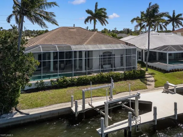 Back of property featuring boat lift, glass enclosure, a water view, a tiled roof, and a lawn