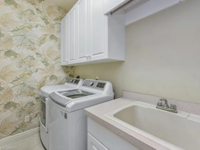 Washroom with tile patterned flooring, a sink, washing machine and clothes dryer, and cabinet space