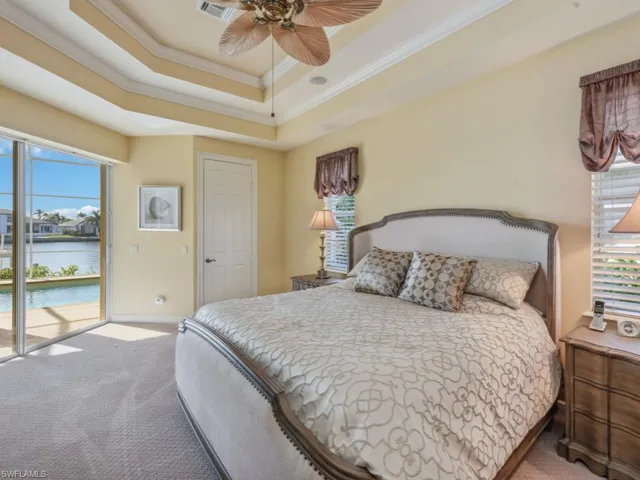 Carpeted bedroom with crown molding, visible vents, access to exterior, a raised ceiling, and a water view