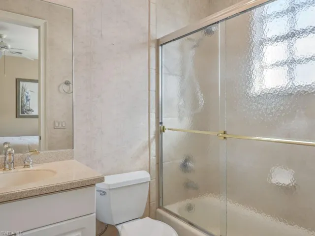 Ensuite bathroom with shower / bath combination with glass door, vanity, ensuite bath, a ceiling fan, and toilet