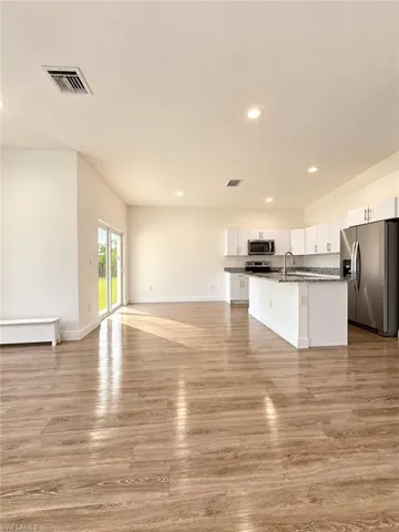 Open-concept area featuring wood-finish flooring, white cabinetry, a stone-surface kitchen island, recessed lighting, and sliding glass doors
