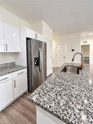 Kitchen featuring stone countertops, white cabinetry with brushed-metal pulls, stainless steel refrigerator, undermount sink with a gooseneck faucet, and wood-finish flooring
