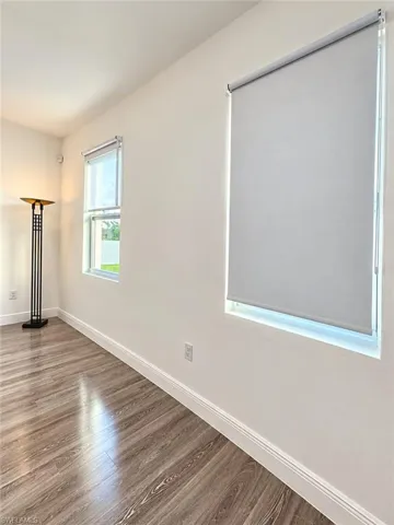 Interior space featuring wood-finish flooring, neutral wall tones, and two windows equipped with roller shades