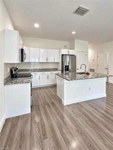Kitchen featuring white cabinetry, stone-finish countertops, stainless steel appliances, a center island with a sink, and wood-finish flooring