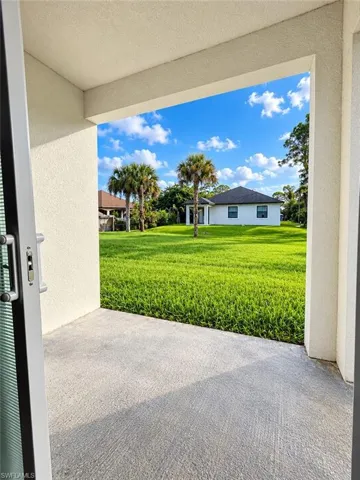Covered concrete patio featuring an expansive lawn, established palm trees, and structural exterior siding
