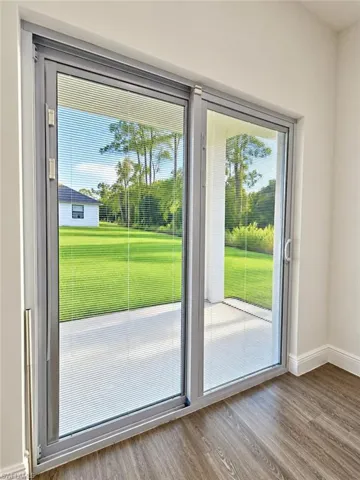 Dual-panel sliding glass doors with integrated blinds, wood-finish flooring, and concrete patio access