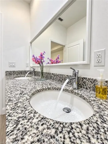 Dual-sink vanity with stone countertop, drop-in oval basins, chrome single-lever faucets, and a full-width wall-mounted mirror
