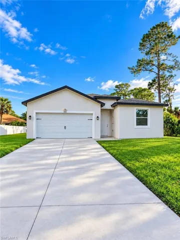 Single-story residence featuring a light-colored stucco exterior, a concrete driveway, a dual-car garage, and a manicured lawn