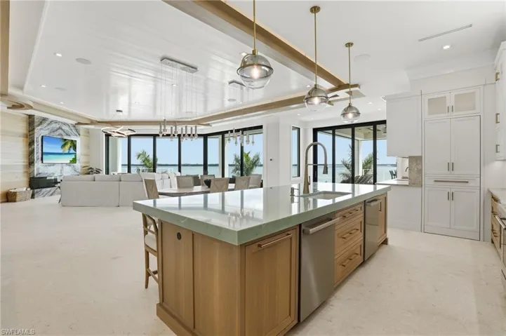 Kitchen with two tone color scheme, open floor plan, a large island with sink, light stone countertops, and pendant lighting - Virtually Edited Image