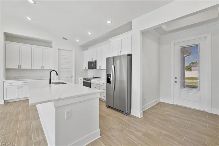 Kitchen with appliances with stainless steel finishes, white cabinets, vaulted ceiling, light stone counters, and a kitchen island with sink
