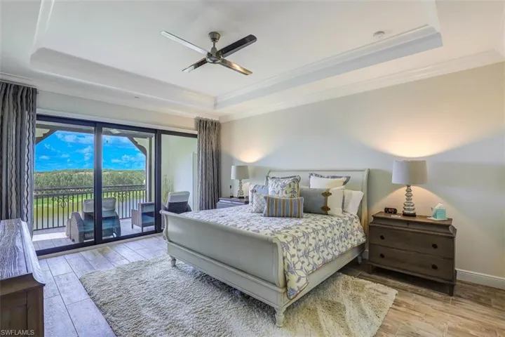 Bedroom with a raised ceiling, wood finished floors, access to exterior, ornamental molding, and a ceiling fan