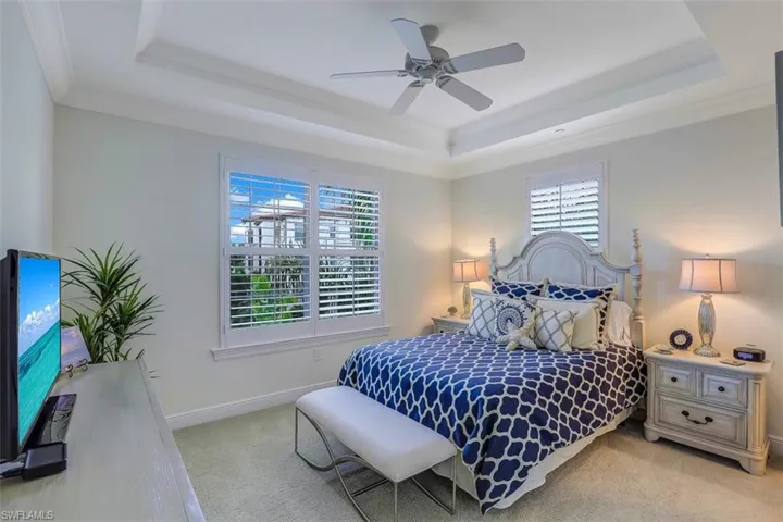 Bedroom with a raised ceiling, multiple windows, ornamental molding, light colored carpet, and a ceiling fan