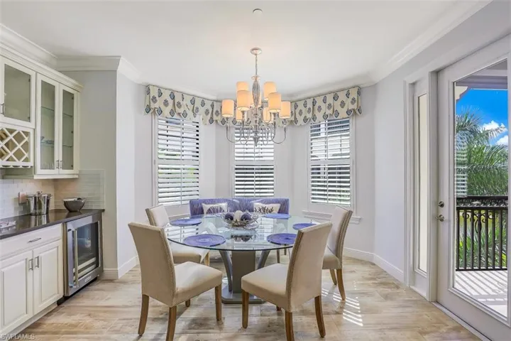 Dining space featuring a chandelier, crown molding, beverage cooler, light wood-style flooring, and a dry bar