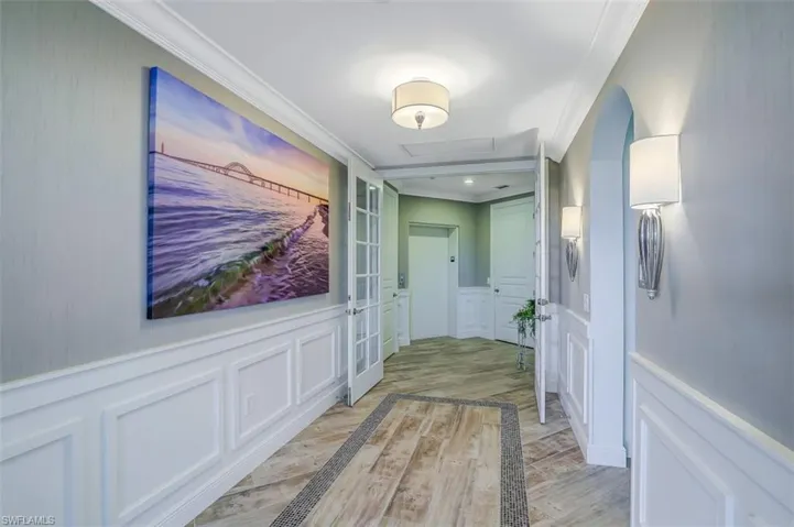 Hallway with a decorative wall, ornamental molding, light wood-style floors, attic access, and wainscoting