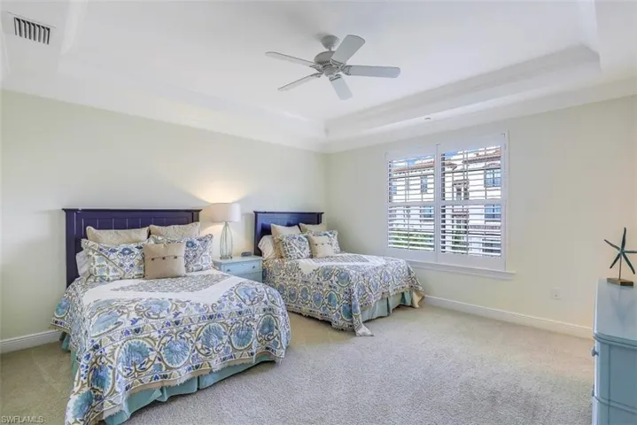 Carpeted bedroom with a raised ceiling, ceiling fan, and crown molding