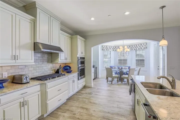 Kitchen featuring arched walkways, a chandelier, backsplash, under cabinet range hood, and recessed lighting