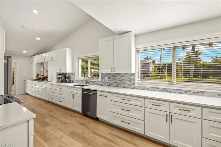 Kitchen featuring stainless steel dishwasher, backsplash, lofted ceiling, white cabinets, and a sink