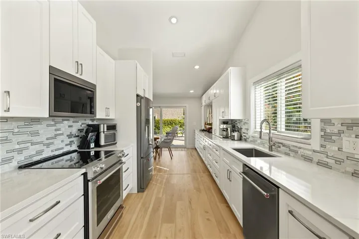 Kitchen with stainless steel appliances, tasteful backsplash, luxury vinyl flooring, and white cabinetry