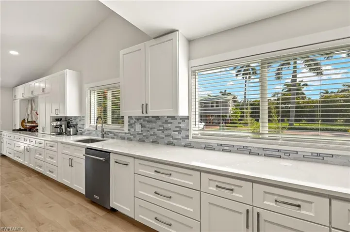 Kitchen featuring stainless steel dishwasher, tasteful backsplash, white cabinetry, and lofted ceiling