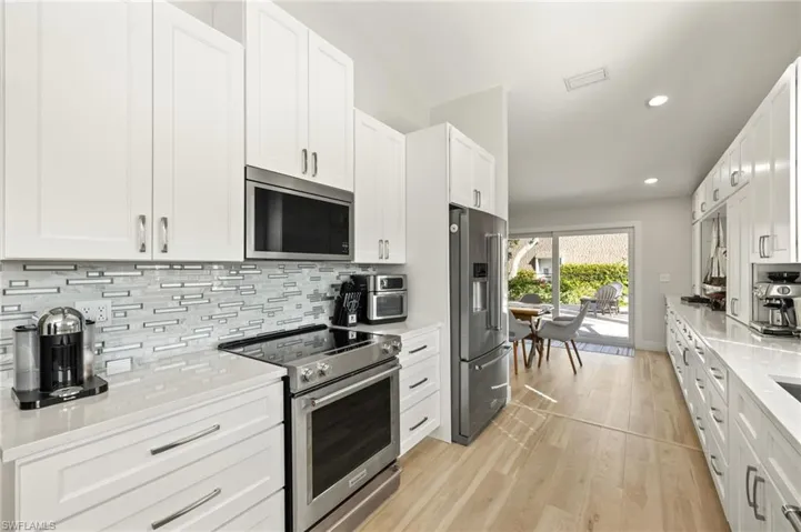 Kitchen featuring appliances with stainless steel finishes, recessed lighting, luxury vinyl floors, decorative backsplash, and white cabinetry