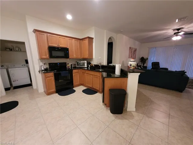 Kitchen featuring washing machine and dryer, black appliances, ceiling fan, and kitchen peninsula