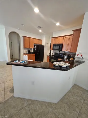 Kitchen with light tile flooring, stove, kitchen peninsula, and black refrigerator