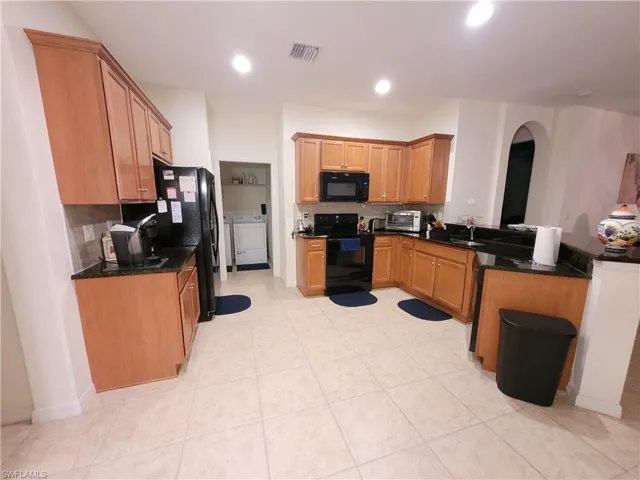 Kitchen with separate washer and dryer, black appliances, dark stone countertops, sink, and light tile floors