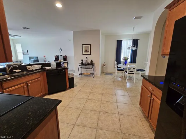 Kitchen featuring hanging light fixtures, black appliances, a notable chandelier, sink, and light tile floors