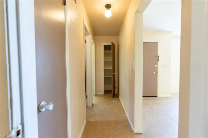 Hallway with tile flooring, featuring an overhead light fixture, light beige wall paint, and a built-in shelving unit