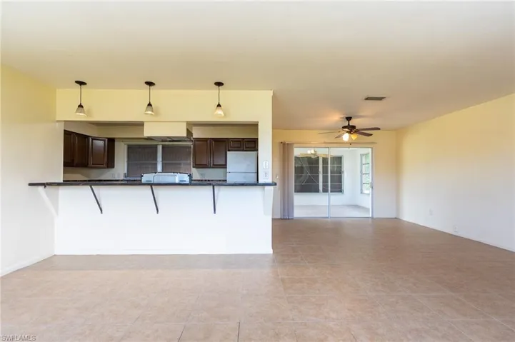Open-concept living and kitchen area featuring tile flooring throughout, dark wood cabinetry with stainless steel appliances, pendant lighting above the kitchen counter, and sliding glass doors providing natural light