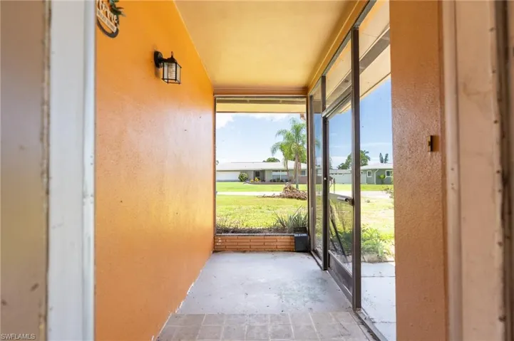 Screened entry porch with a tiled floor, exterior wall sconce, and brick planter box