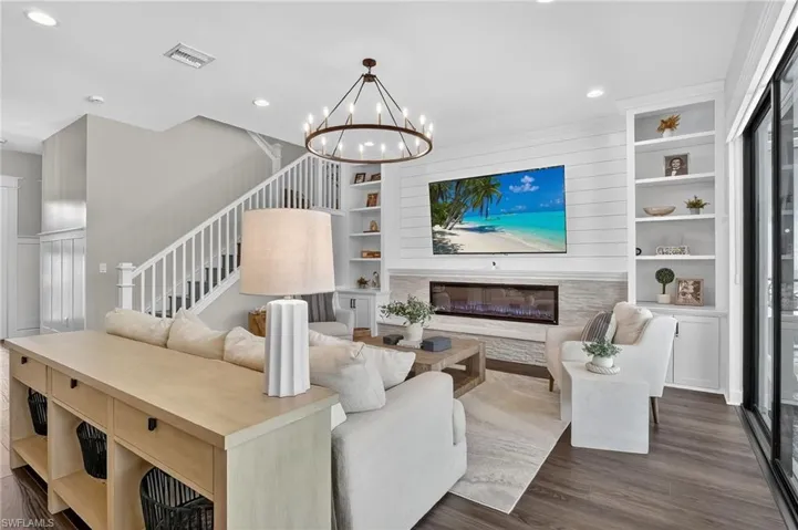 Living area with built in shelves, a glass covered fireplace, dark wood-type flooring, stairs, and recessed lighting