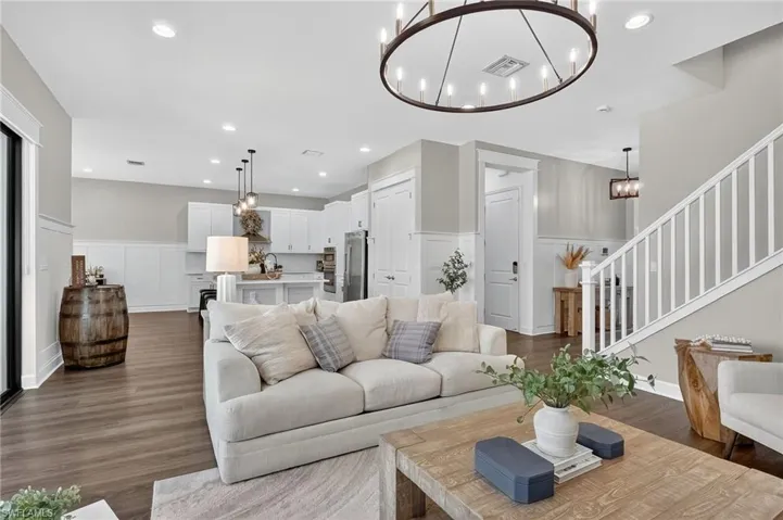 Living area with a decorative wall, a wainscoted wall, a chandelier, stairs, and dark wood-type flooring