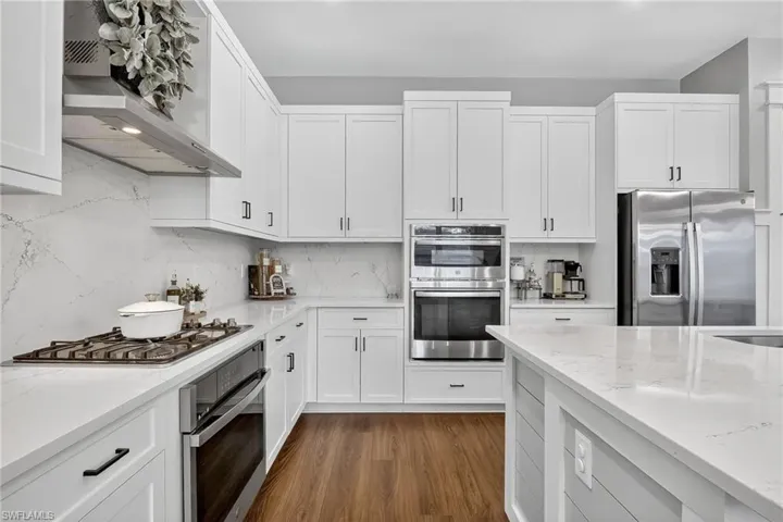 Kitchen with tasteful backsplash, stainless steel appliances, white cabinets, and light stone countertops
