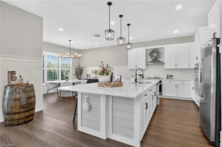 Kitchen featuring white cabinets, hanging light fixtures, dark wood finished floors, light stone counters, and an island with sink