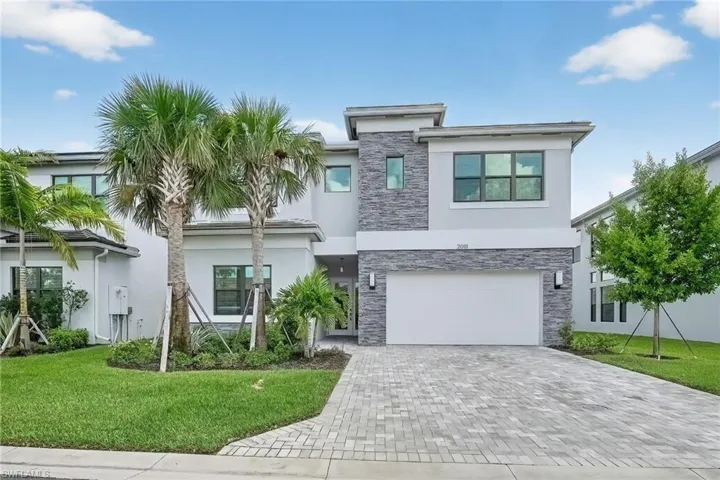 Modern home with stone siding, a front yard, decorative driveway, and stucco siding