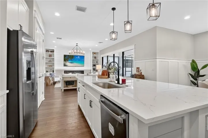 Kitchen with white cabinets, appliances with stainless steel finishes, light stone countertops, decorative light fixtures, and recessed lighting