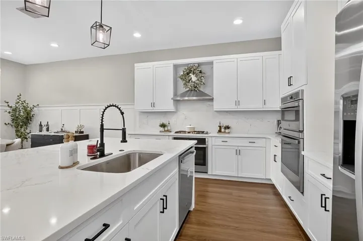 Kitchen with white cabinets, decorative light fixtures, backsplash, stainless steel appliances, and recessed lighting