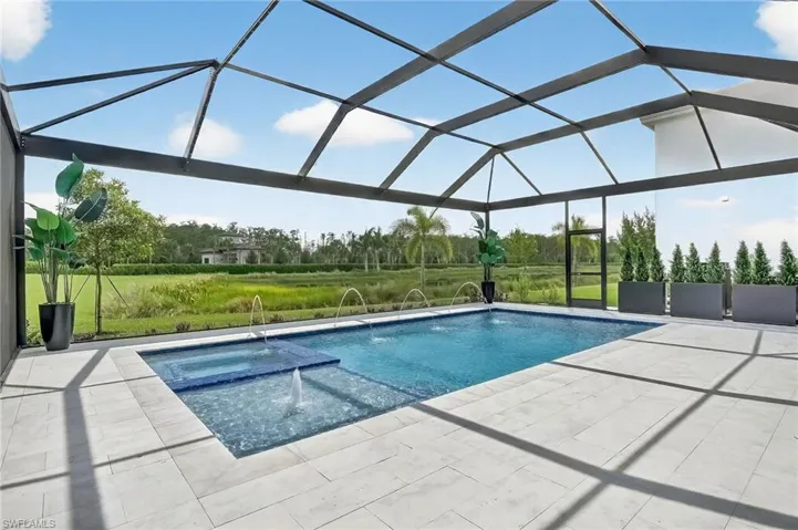 View of swimming pool featuring a lawn, glass enclosure, a sunroom, a pool with connected hot tub, and a patio