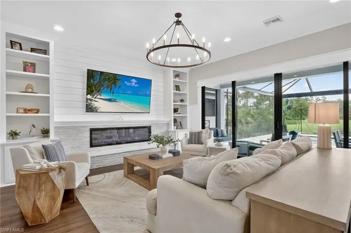 Living room with built in shelves, a glass covered fireplace, wood finished floors, a sunroom, and recessed lighting