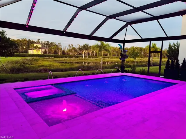 View of pool with a water view, glass enclosure, and a pool with connected hot tub