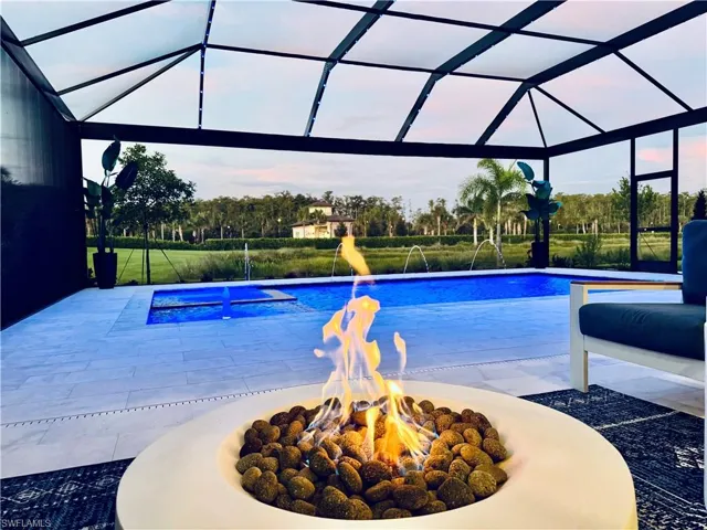 View of swimming pool featuring a sunroom, glass enclosure, a patio area, a pool with connected hot tub, and an outdoor fire pit