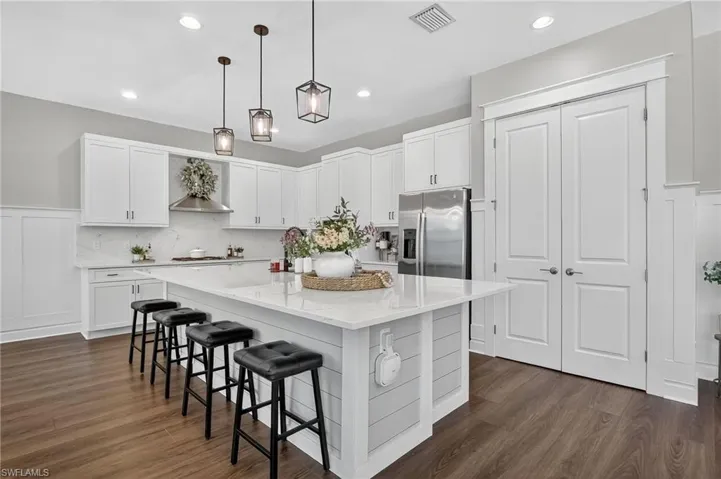 Kitchen with a breakfast bar, decorative light fixtures, white cabinets, a kitchen island, and stainless steel refrigerator with ice dispenser